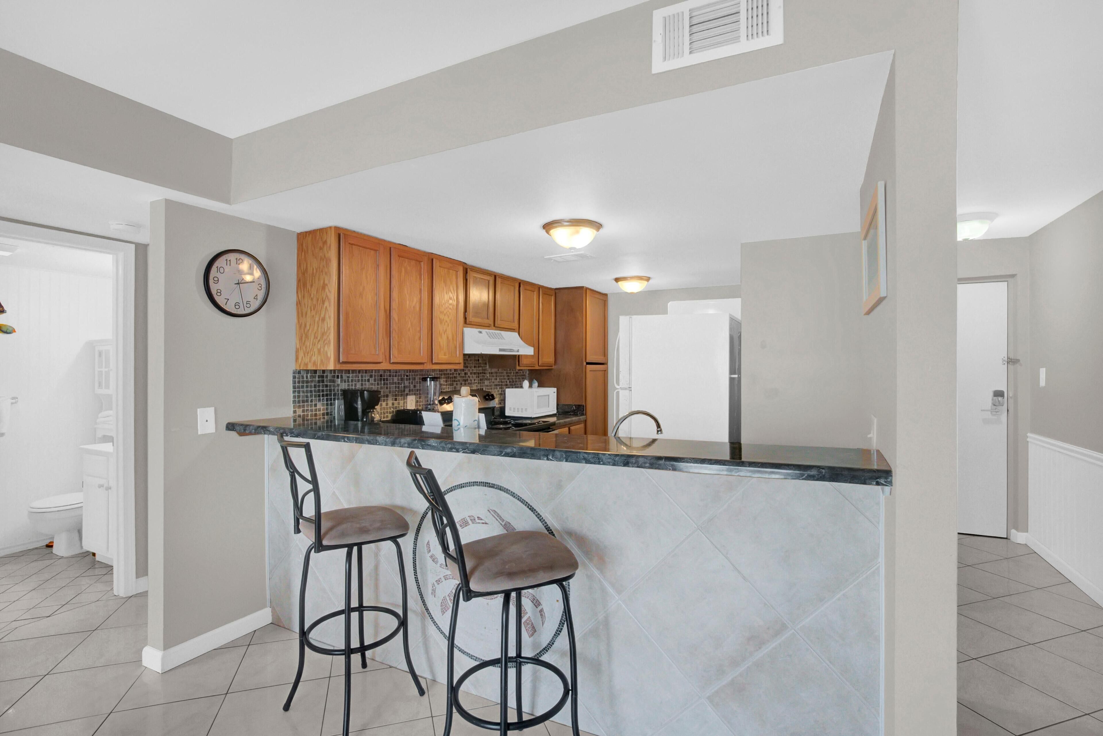 A modern kitchen with wooden cabinets, a marble countertop, and two bar stools.