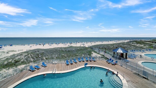 A pool area with lounge chairs and a view of the beach. - Sugar Beach 241 (Orange Beach)