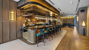 A modern bar area with a long counter, multiple stools, and a variety of bottles and glasses. - 601 RESIDENCES SKY FLOOR 1BR UNIT #2611 (Miami)