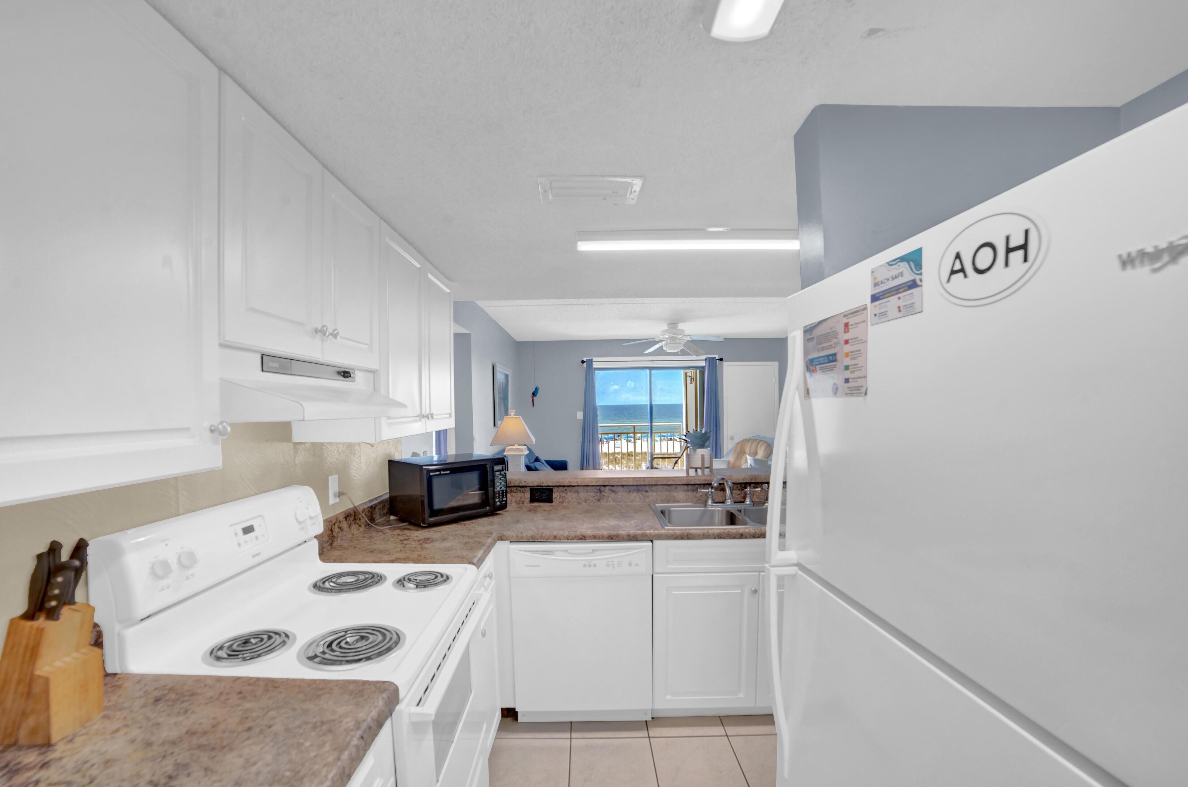 Une cuisine moderne avec des armoires blanches, une cuisinière, un four à micro-ondes et un lave-vaisselle. Une fenêtre offre une vue sur la plage.