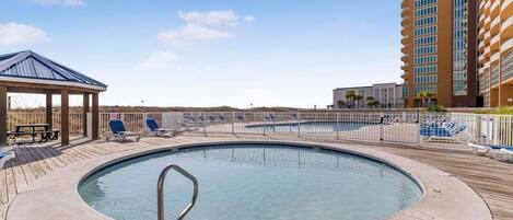 A rooftop pool with a wooden deck, lounge chairs, and a covered seating area.