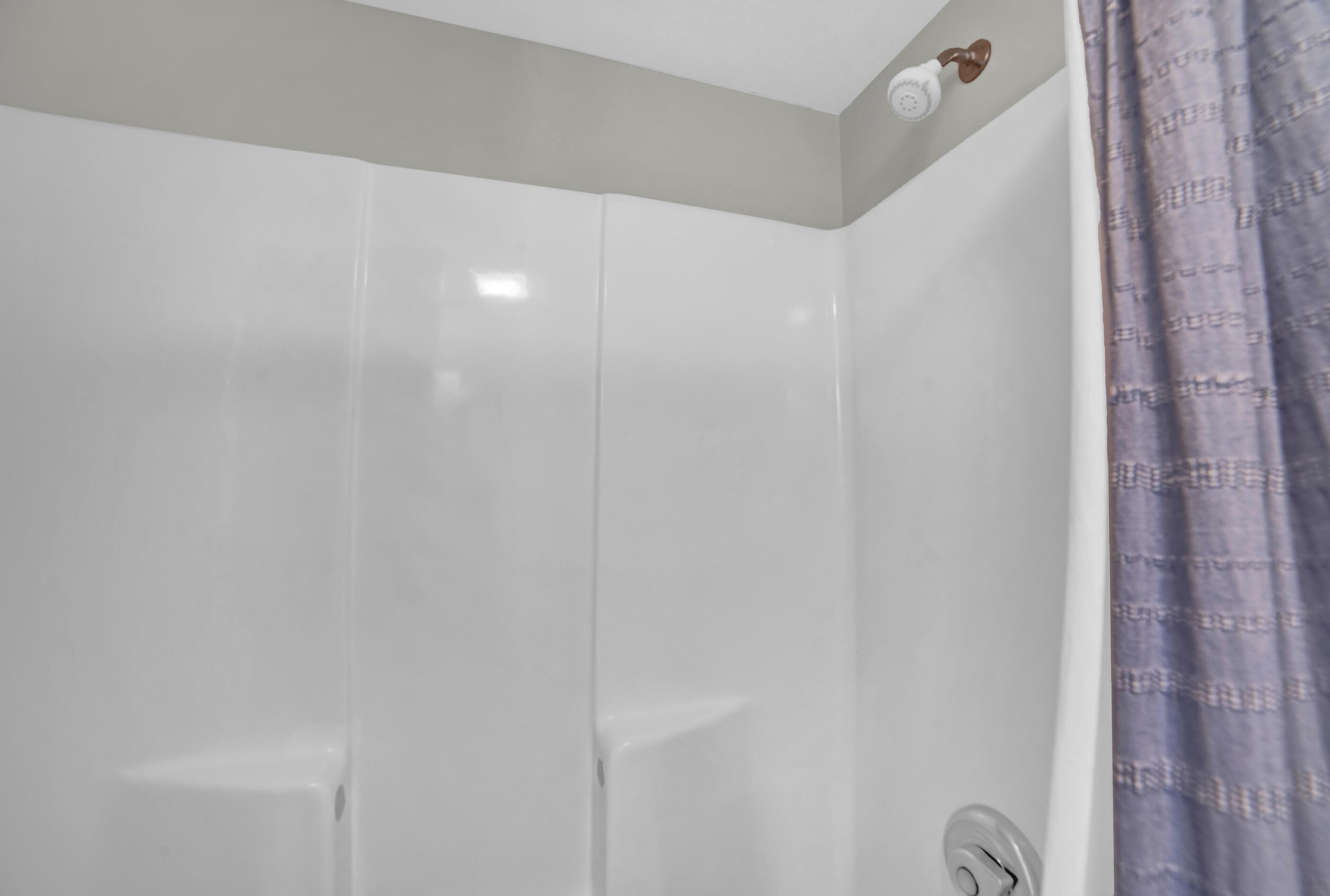 Un baño con paredes blancas, cortina de ducha y cabezal de ducha visible.