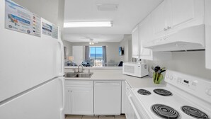 A modern kitchen with white appliances, a dishwasher, and a microwave. There are cabinets and a window with a view. - Sugar Beach 246 (Orange Beach)