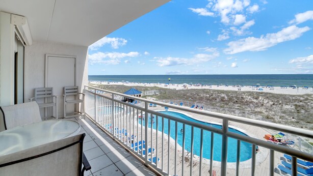A balcony with a view of a beach, a pool, and lounge chairs. - Sugar Beach 246 (Orange Beach)