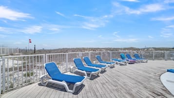 A wooden deck with blue lounge chairs and a white railing.