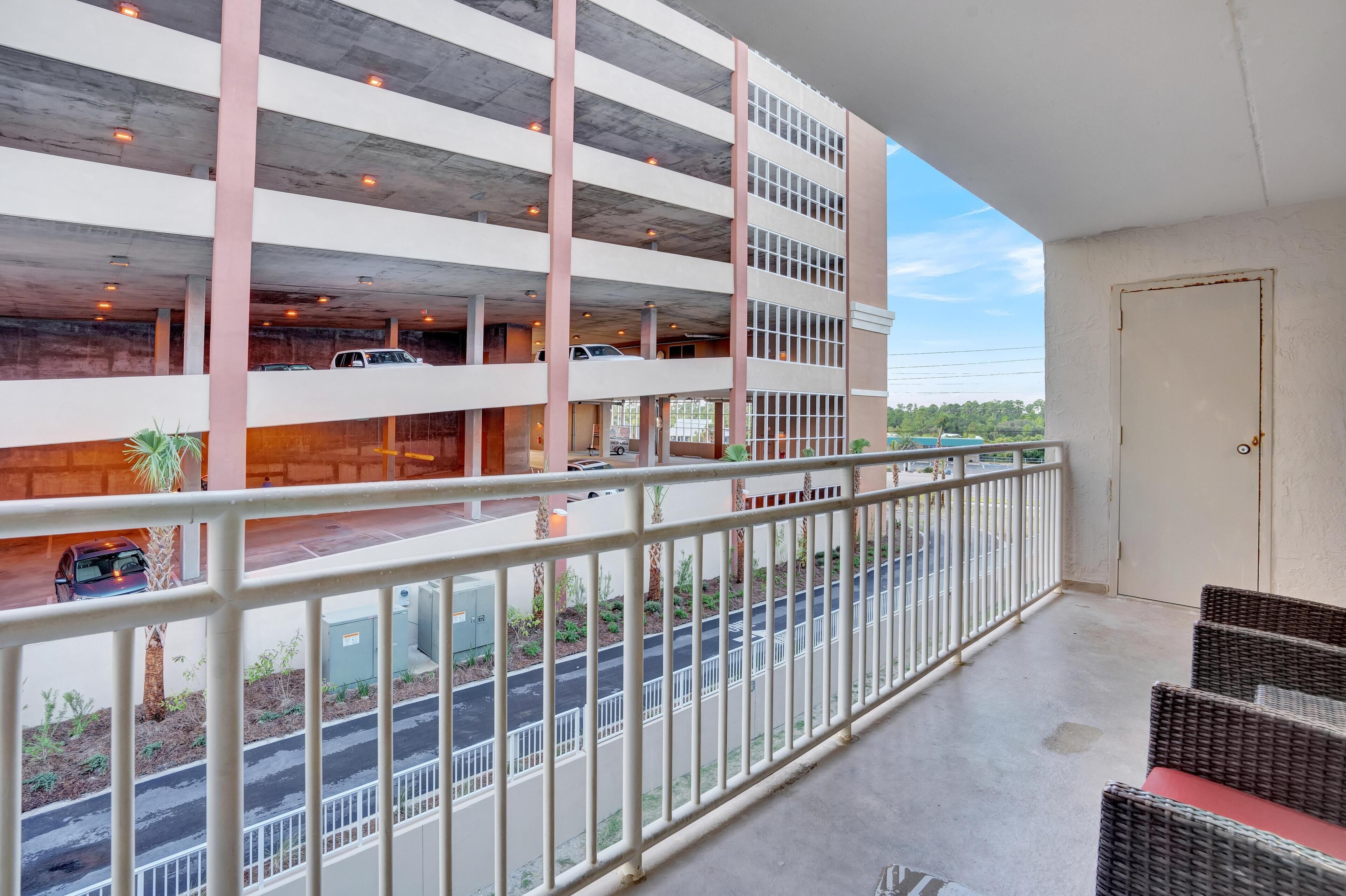A multi-level parking structure with vehicles parked on different levels, a balcony with a railing, and a view of the street below.