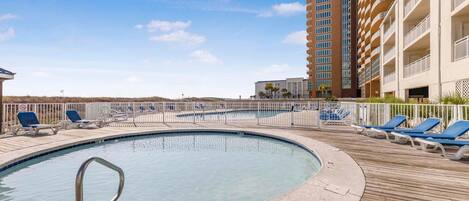 A pool area with lounge chairs and a tall building in the background.