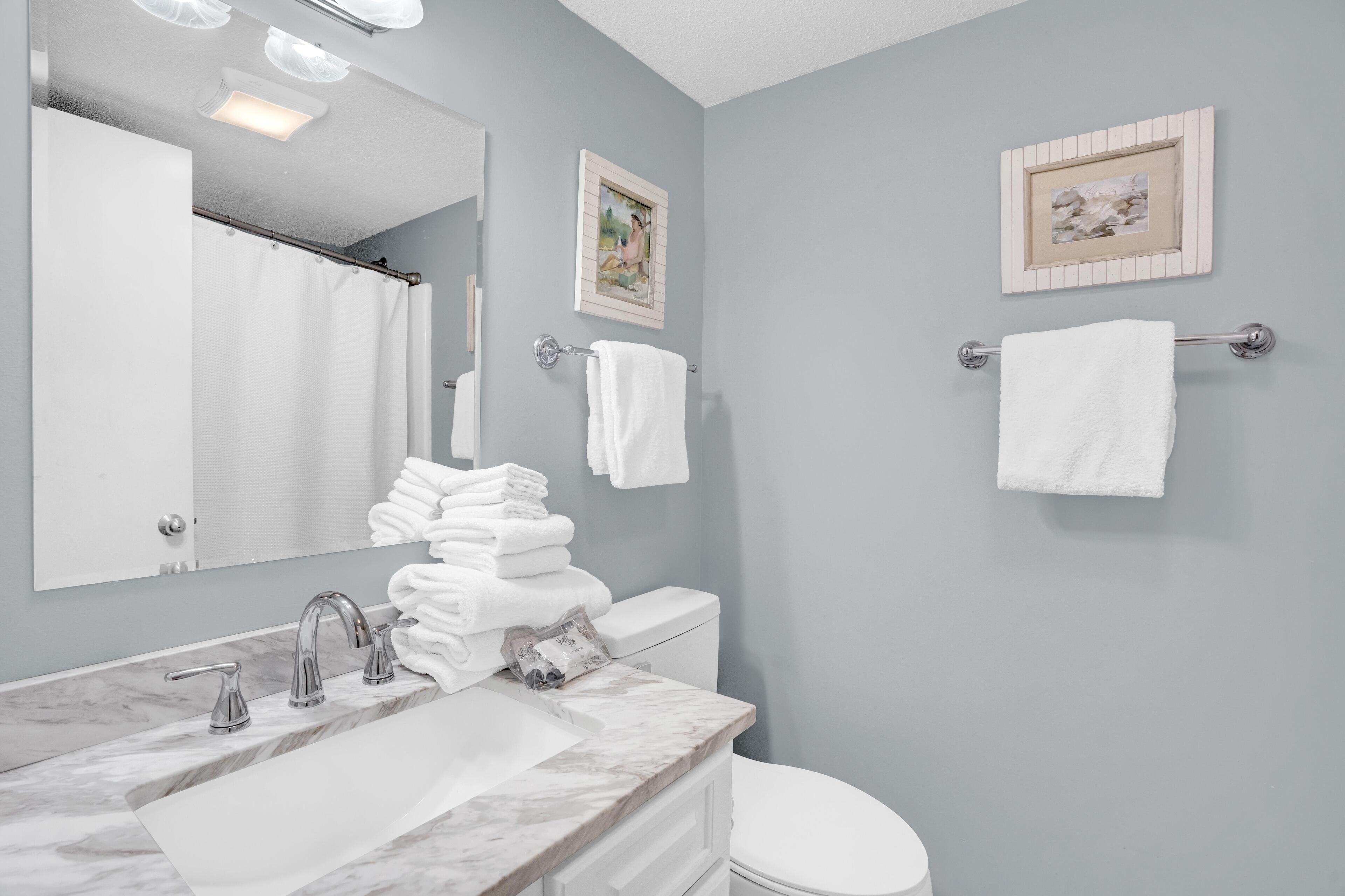 A bathroom with a marble sink, a toilet, and two framed pictures on the wall.