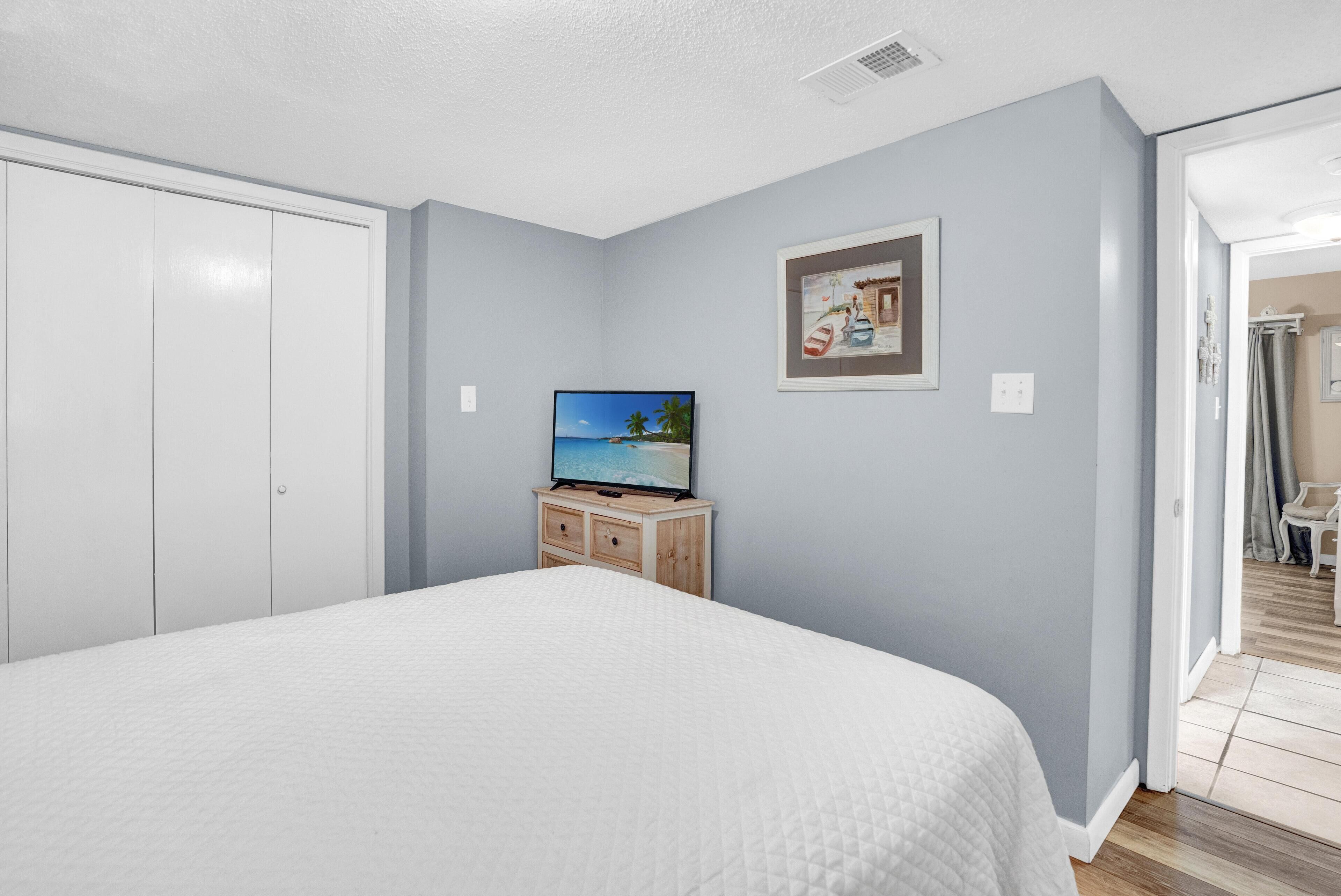 A bedroom with a bed, a TV on a wooden cabinet, and a painting on the wall.