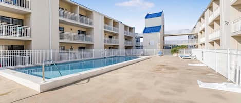 Area piscina di un hotel con una lunga vasca, diversi balconi e un edificio centrale con tetto blu.