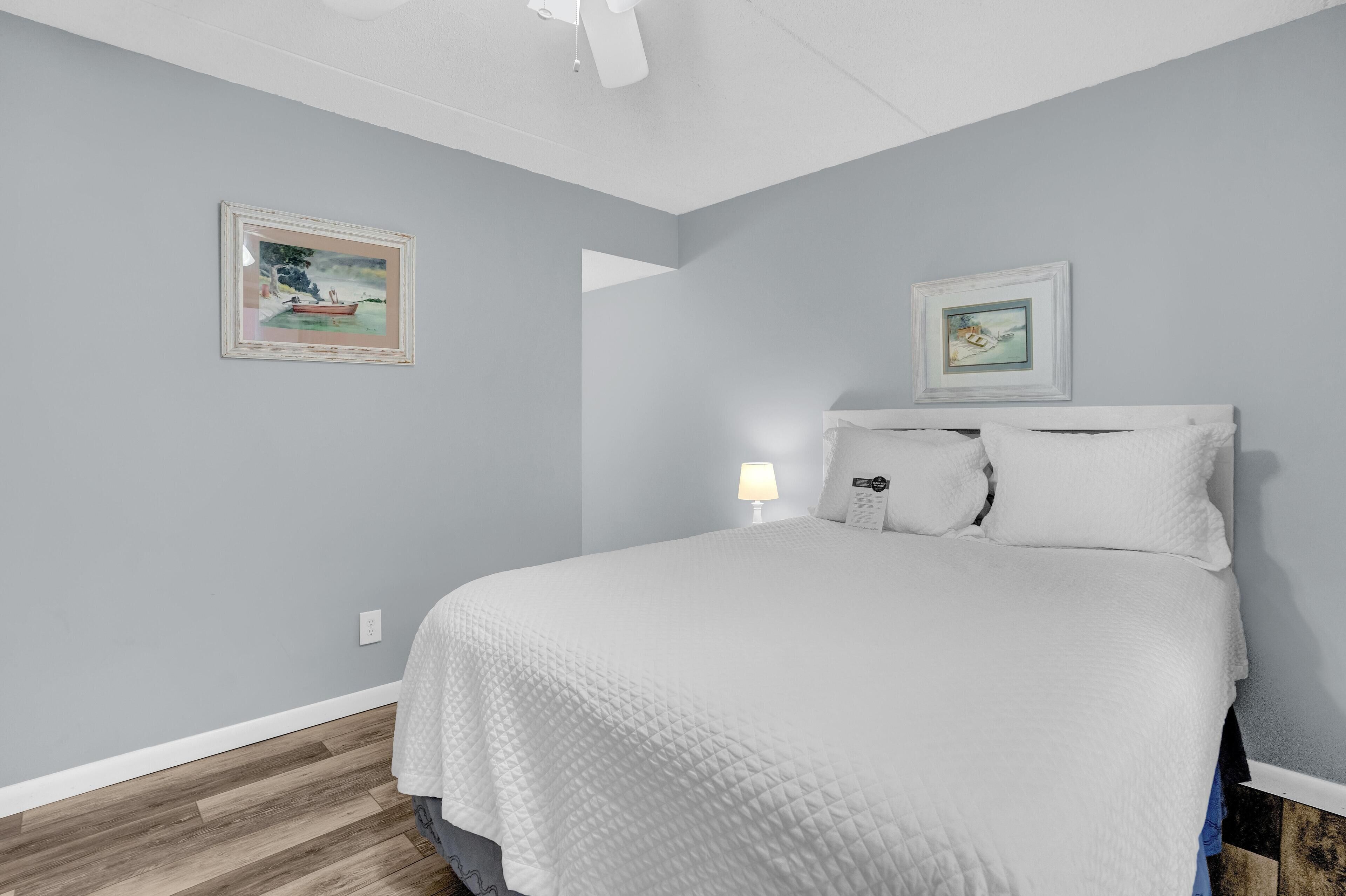 Un dormitorio con una cama, dos cuadros en la pared, una lámpara de noche y suelo de madera.