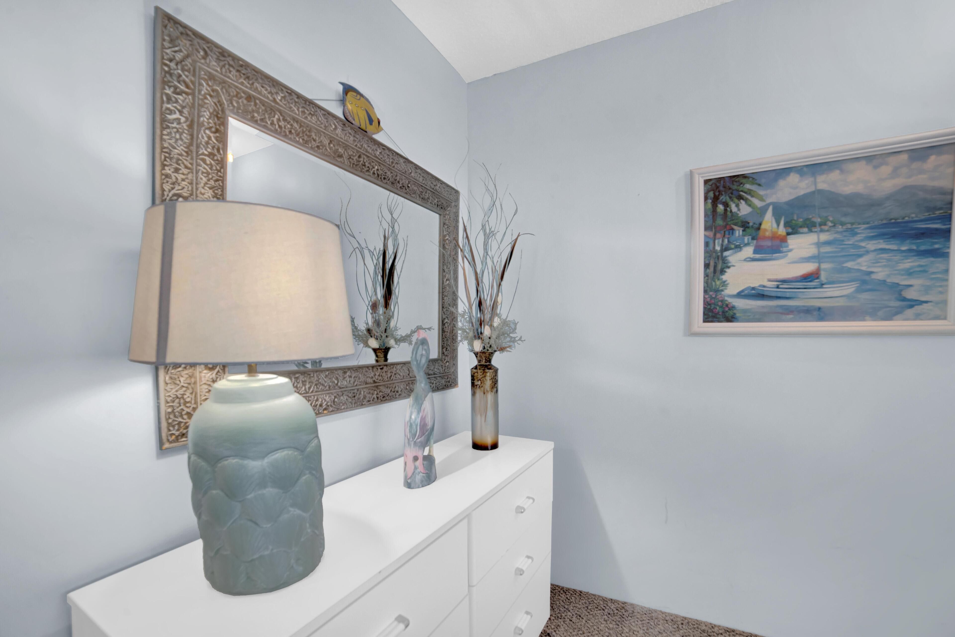 A room with a white dresser, a large mirror, a lamp, and a painting of a beach scene.
