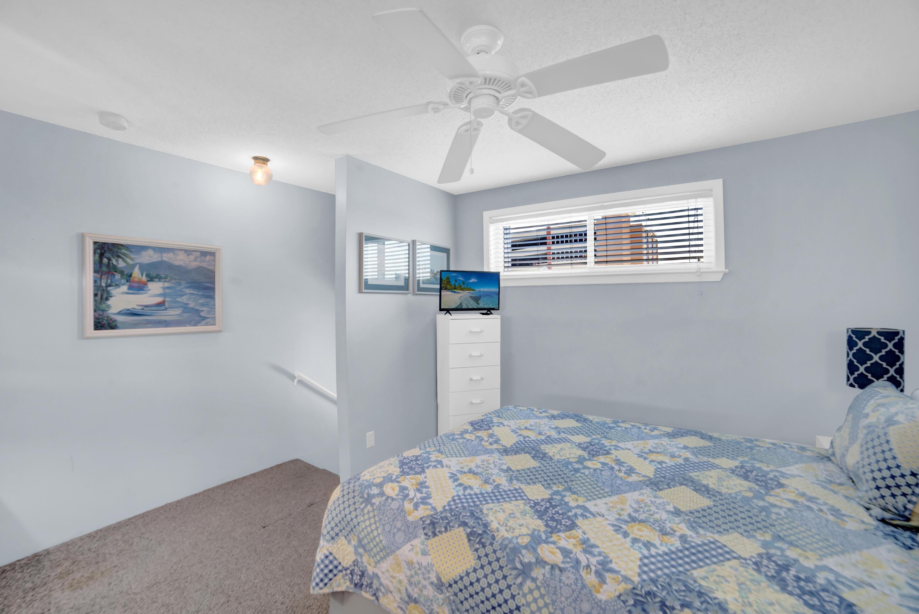 Une chambre à coucher avec un lit, un ventilateur de plafond, des stores aux fenêtres et un tableau accroché au mur.