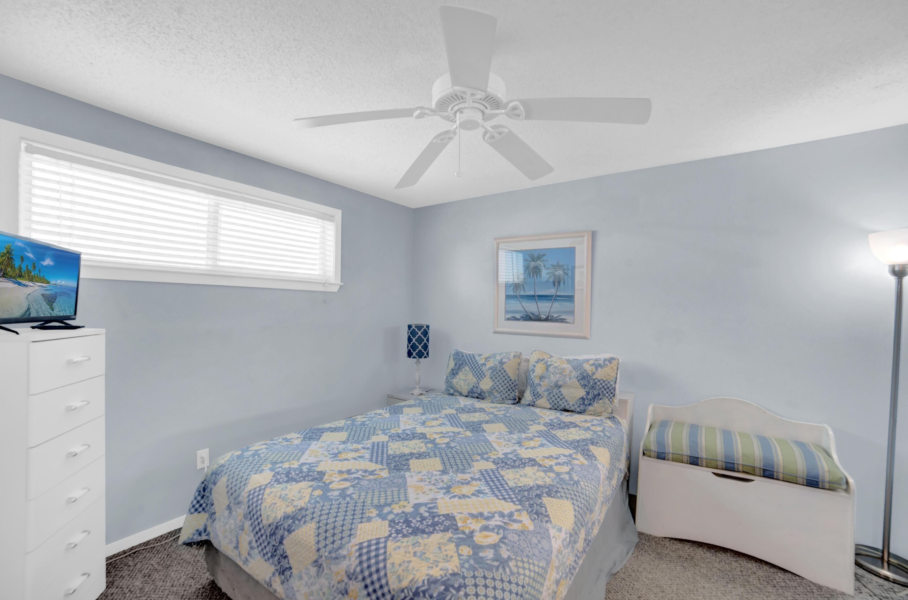 A bedroom with a bed, a dresser, a ceiling fan, a window with blinds, and a framed picture on the wall.
