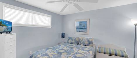 A bedroom with a bed, a dresser, a ceiling fan, a window with blinds, and a framed picture on the wall.