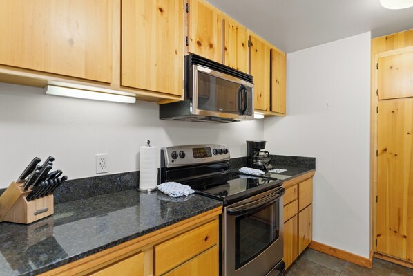 A kitchen with wooden cabinets, a stainless steel microwave, a stove, and a coffee maker.