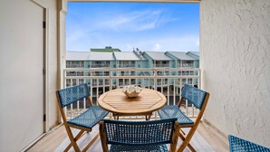 A balcony with a round wooden table, two blue woven chairs, and a white bowl. - Sugar Beach 323 (Orange Beach)