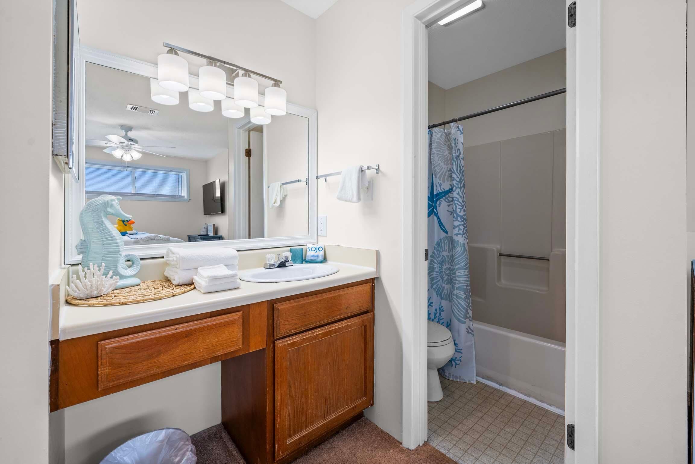 A bathroom with a wooden vanity, a large mirror, and a shower with a blue shower curtain.