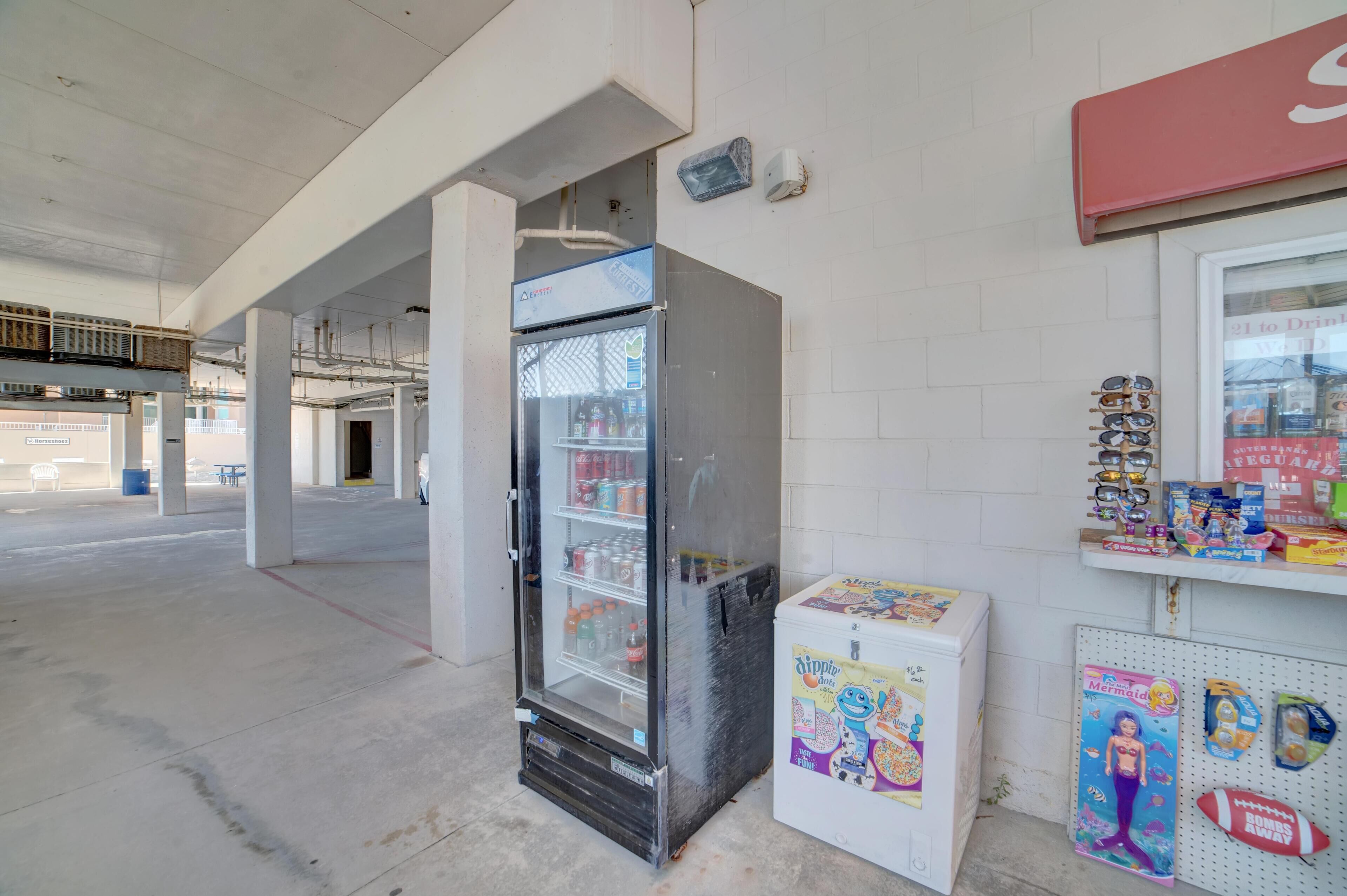 A commercial space with a refrigerated display case, a small refrigerator, and a shelf with various items including sunglasses and snacks.