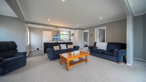 A spacious living room with a large wooden coffee table, two dark blue sofas, and a kitchen in the background.