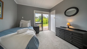 A bedroom with a bed, a dresser, a lamp, and a sliding glass door leading to a balcony.