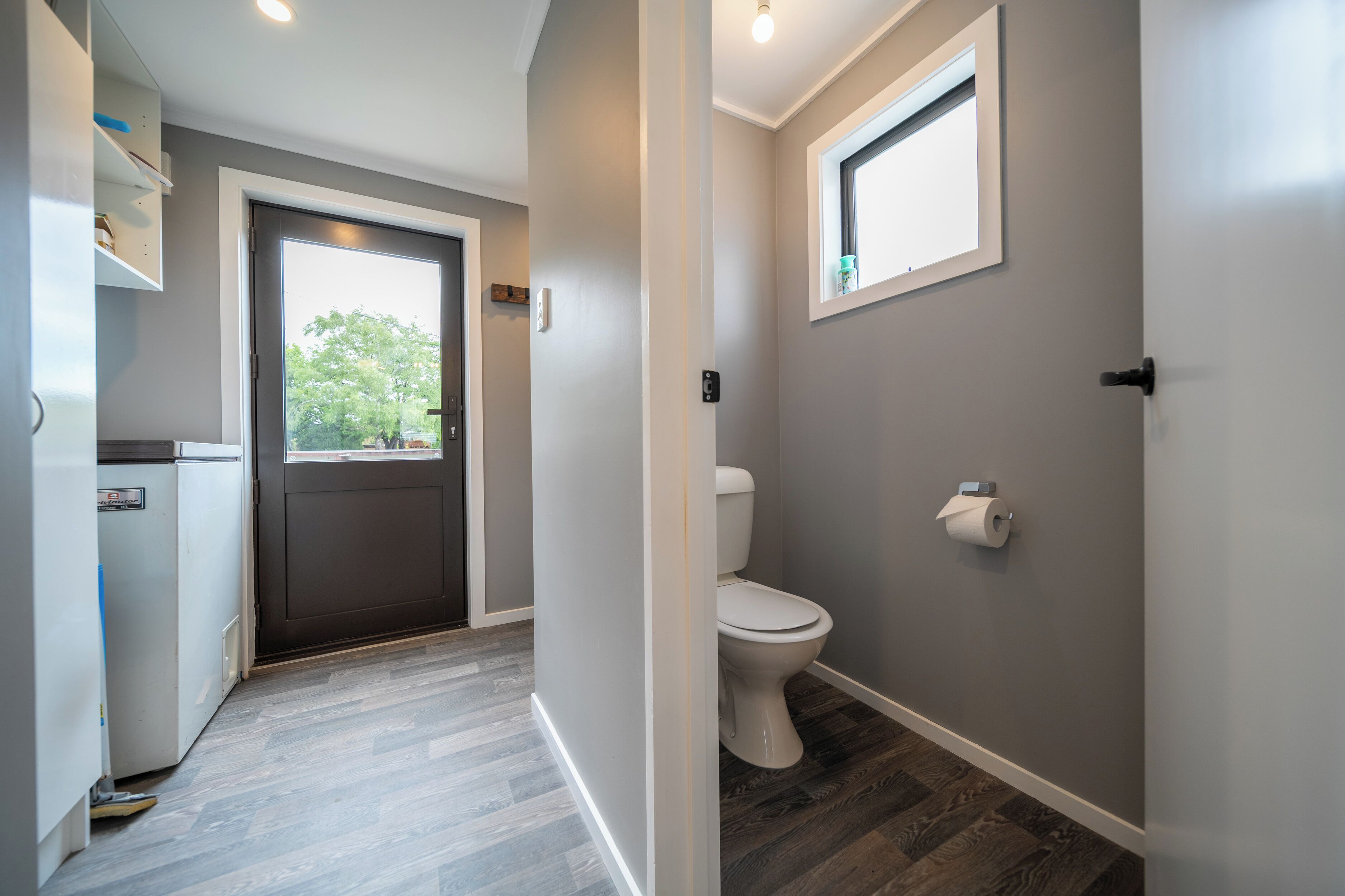 Une salle de bain moderne équipée de toilettes, d’une fenêtre et d’une porte donnant sur un espace cuisine.