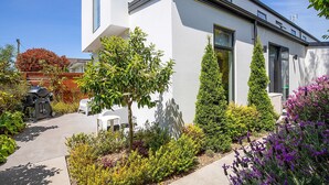 Una casa moderna con un jardín cuidado, una zona de barbacoa y cielo despejado.