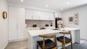 Una cocina moderna con armarios blancos, una salpicadura de mármol y una isla central con dos taburetes de madera.