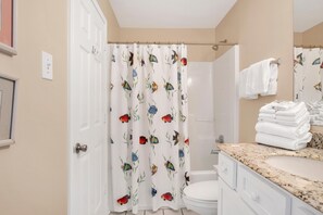 A bathroom with a shower curtain featuring a fish pattern, a white toilet, a sink with a granite countertop, and a mirror above the sink. - Tradewinds 1305 (Orange Beach)