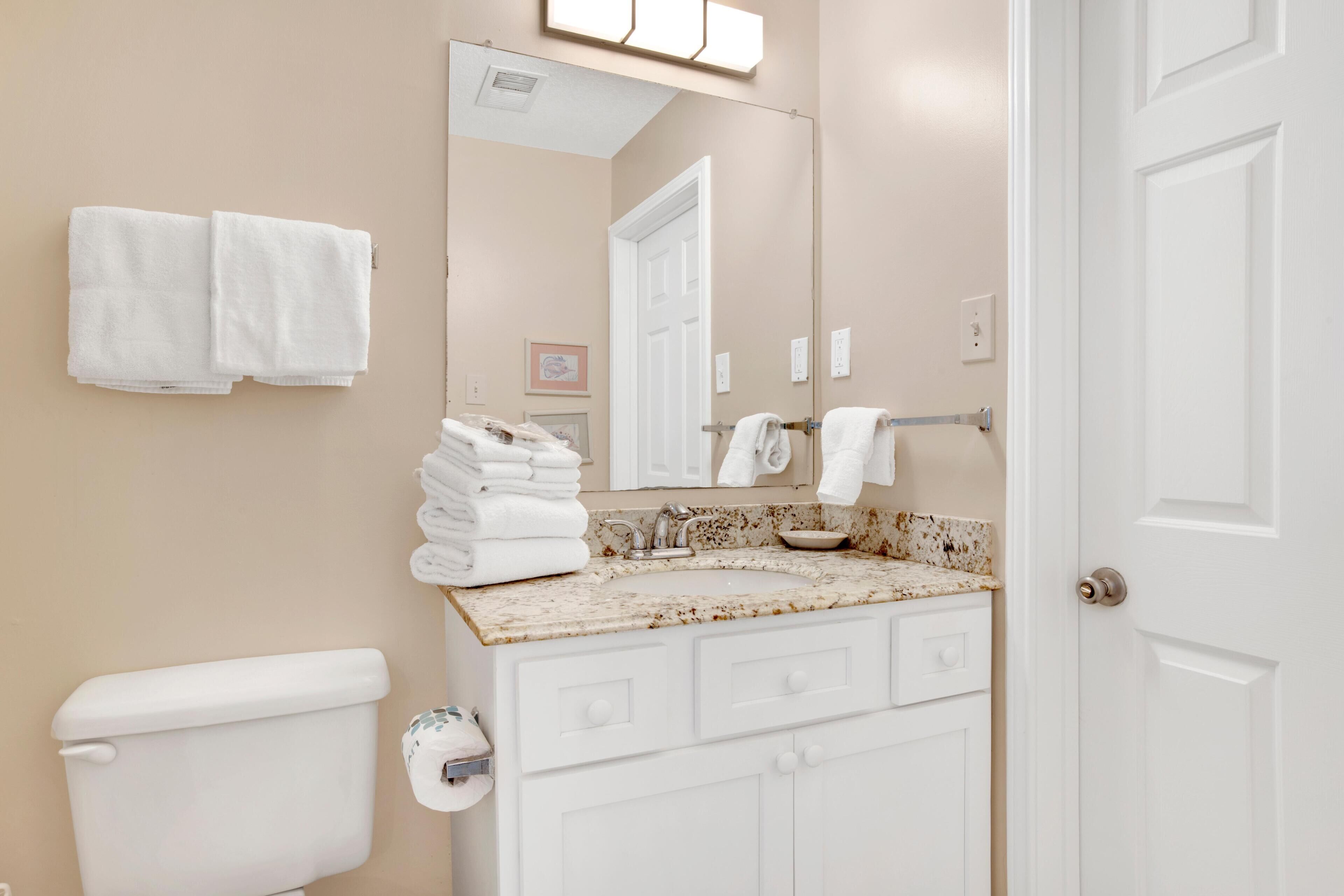 A bathroom with a toilet, sink, and mirror. There are towels hanging on the wall and a door to the right.