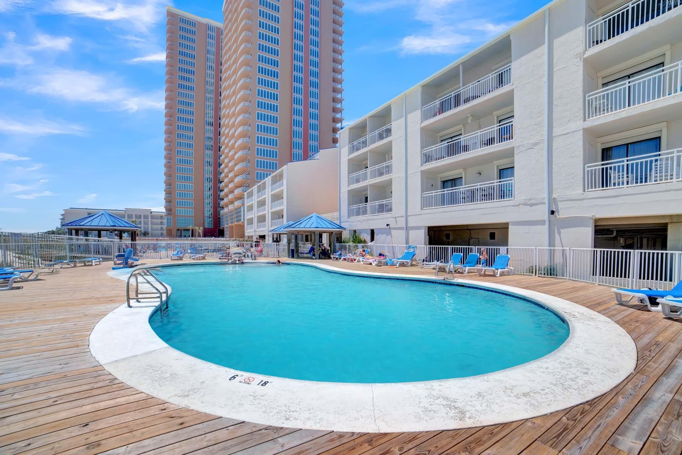 A pool area with a wooden deck, lounge chairs, and a view of tall buildings in the background.