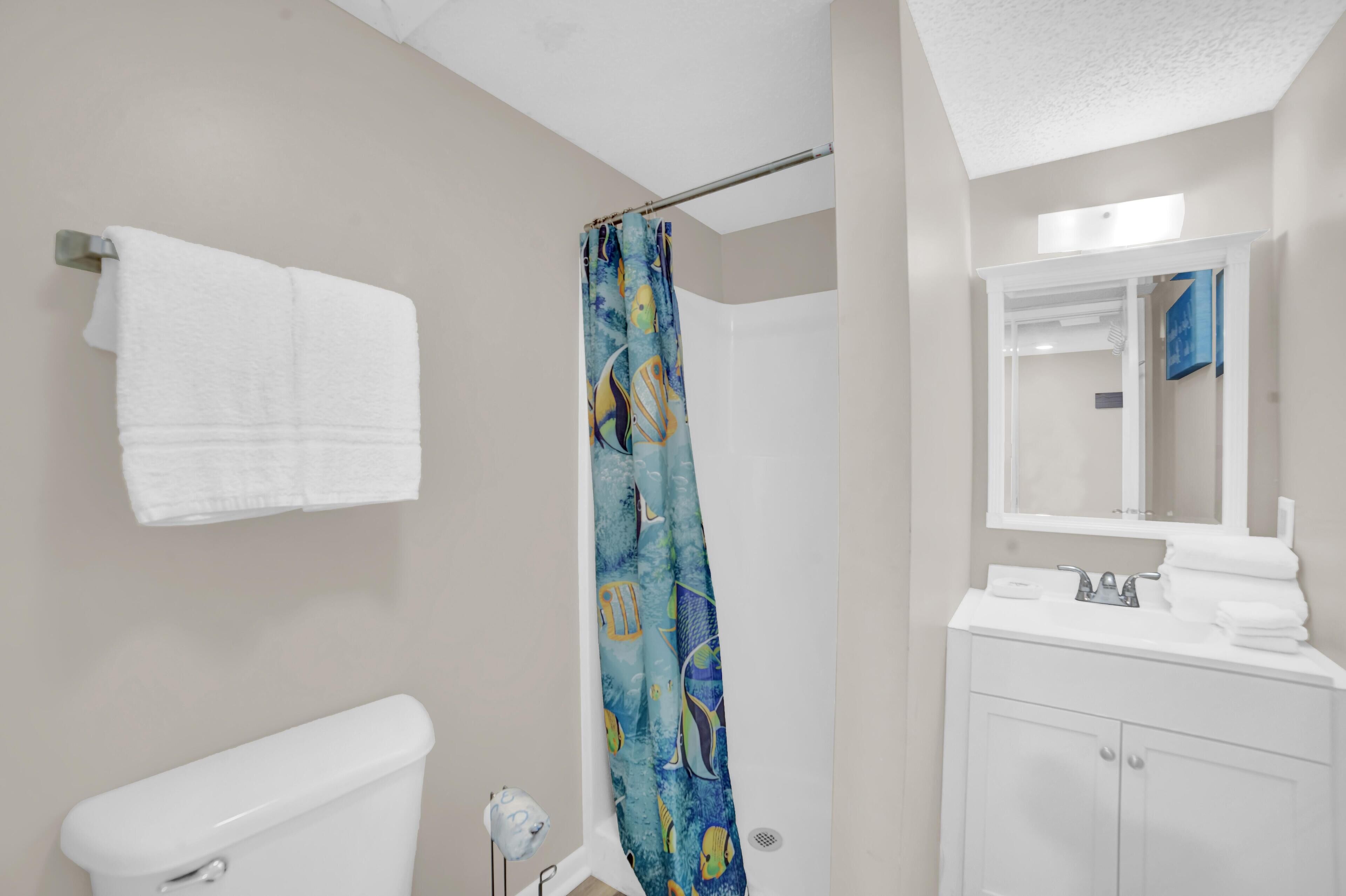 A bathroom with a toilet, a shower with a blue patterned curtain, a sink with a mirror, and a towel rack with two white towels.