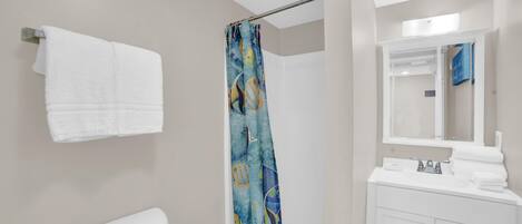 A bathroom with a toilet, a shower with a blue patterned curtain, a sink with a mirror, and a towel rack with two white towels.
