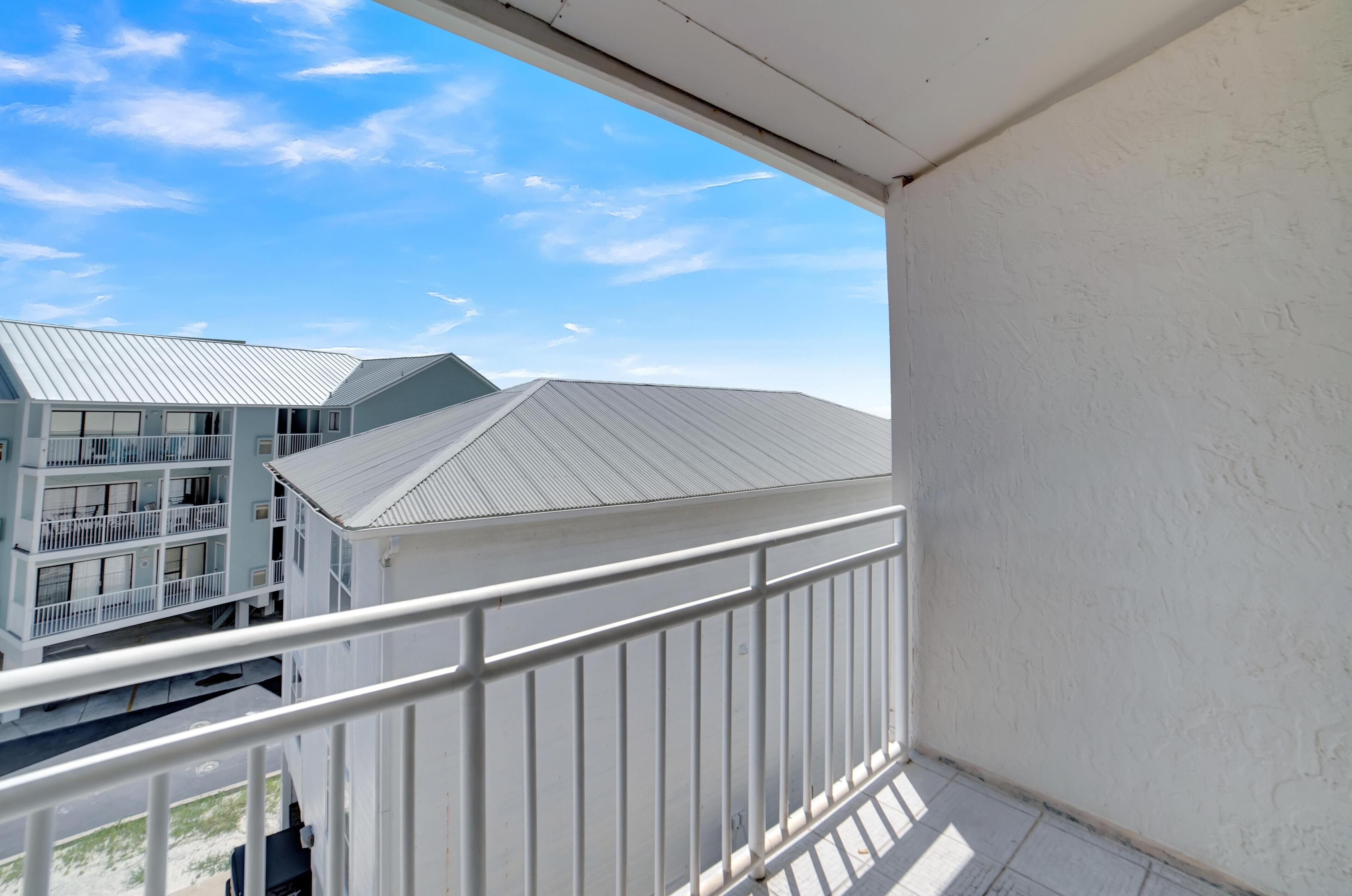 A balcony with a white railing overlooking a building with multiple balconies and a metal roof.