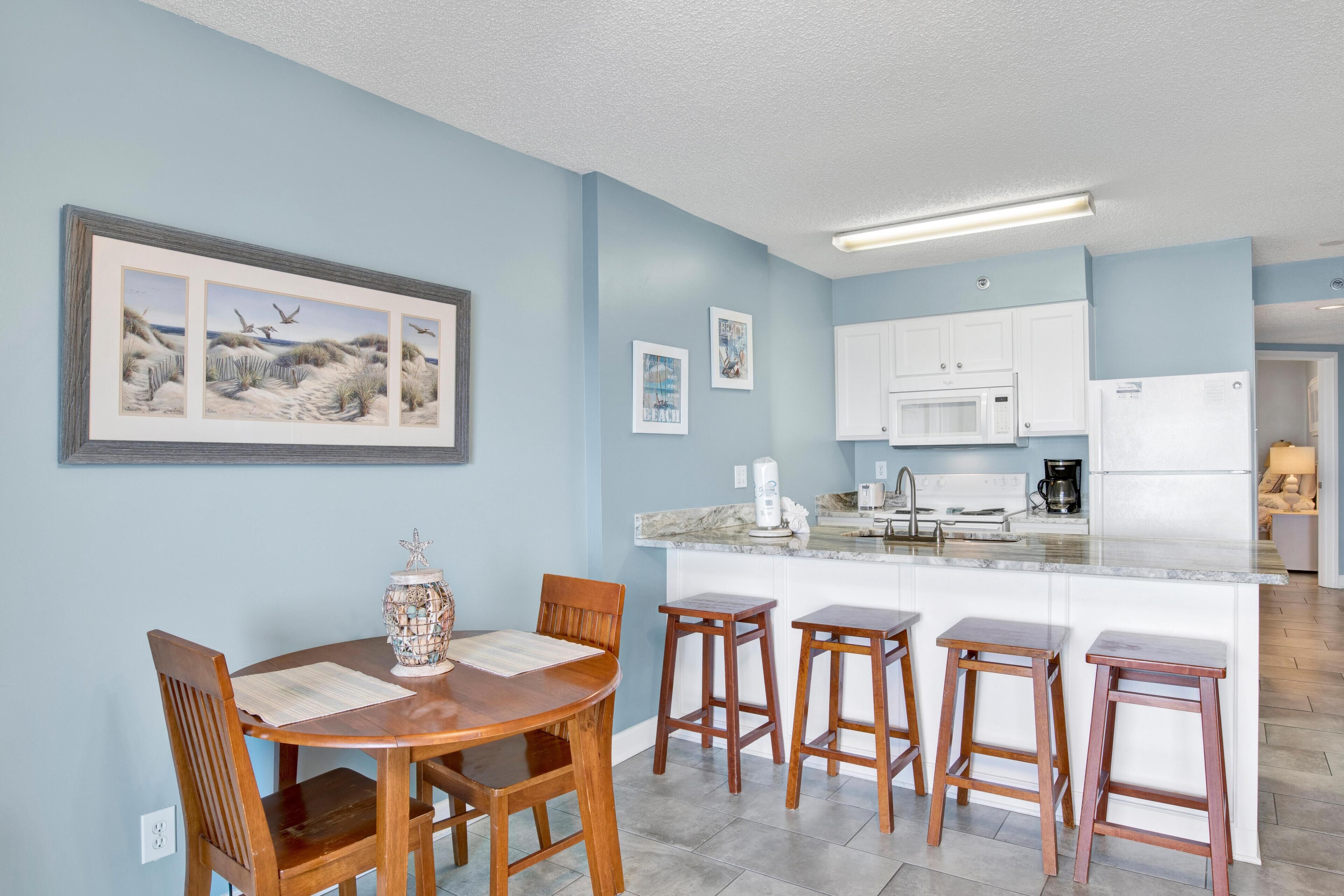 A modern kitchen with white cabinets, a central island with stools, and a dining area with wooden chairs and a table.