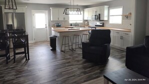 A modern kitchen with a central island, bar stools, and a black chair. - Close to Lake G’VILLE 3-BR house with AC, BOAT BARN-24’x48’, WiFi in Albertville (Albertville)