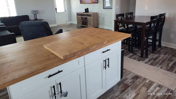 A modern kitchen with a wooden countertop, white cabinets, and a dining area with a dark wooden table and chairs. - Close to Lake G’VILLE 3-BR house with AC, BOAT BARN-24’x48’, WiFi in Albertville (Albertville)