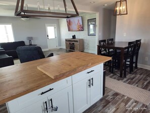 A modern kitchen with a wooden countertop, white cabinets, and a dining area with a dark wooden table and chairs.