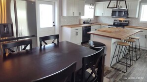 A modern kitchen with white cabinets, stainless steel appliances, a wooden dining table, and bar stools. - Close to Lake G’VILLE 3-BR house with AC, BOAT BARN-24’x48’, WiFi in Albertville (Albertville)