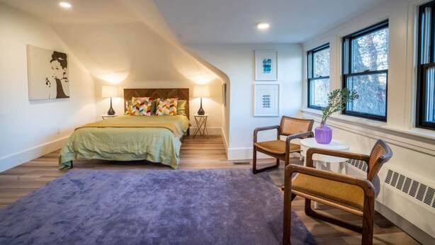 A bedroom with a bed, two chairs, a small table, and a window with a view. - The Buckeye Retreat Mansion (Columbus)