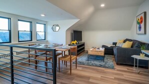 A modern living room with a dining area, large windows, a flat-screen TV, and a cozy sofa. - The Buckeye Retreat Mansion (Columbus)