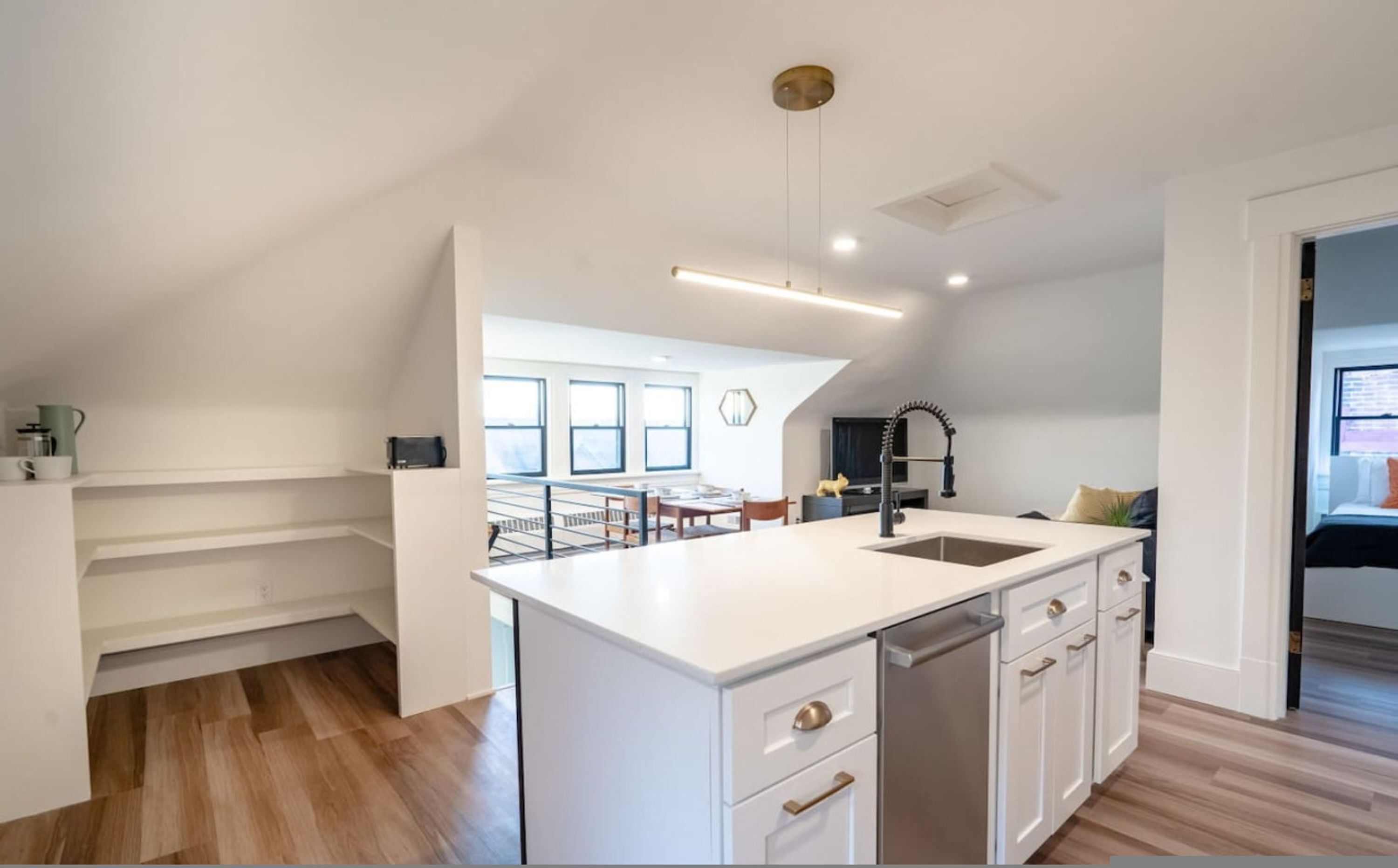 A modern kitchen with white cabinetry, a central island, and a view to a dining area.