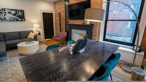 A modern living room with a brick wall, a fireplace, a dining table with chairs, a sofa, and a TV mounted on the wall. - The Buckeye Retreat Mansion (Columbus)
