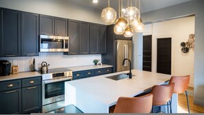 A modern kitchen with dark cabinets, stainless steel appliances, a large island, and pendant lighting. - The Buckeye Retreat Mansion (Columbus)