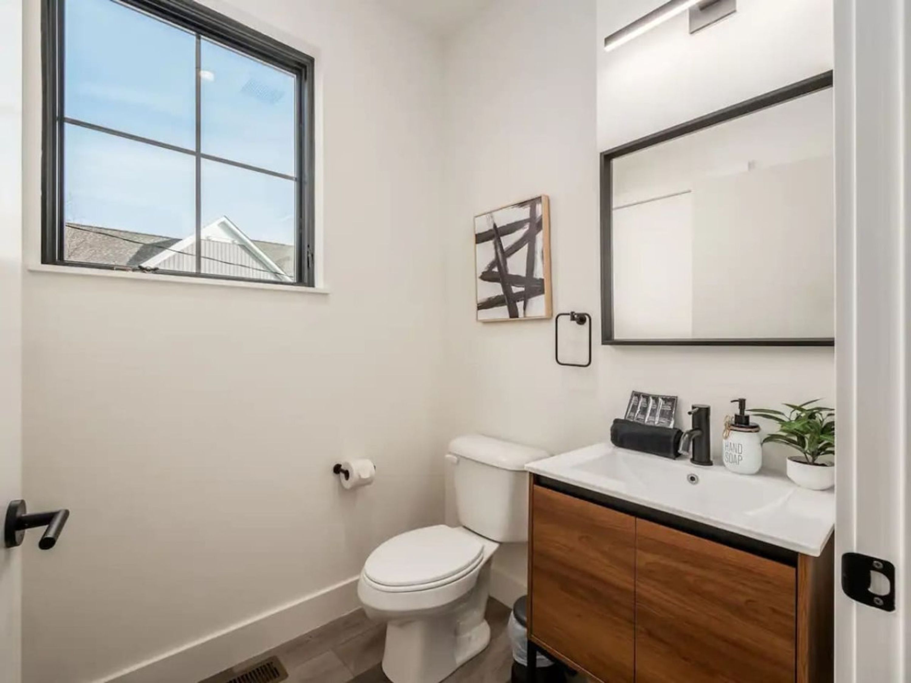 Ein modernes Badezimmer mit Toilette, Waschbecken mit Spiegel und einem Fenster.