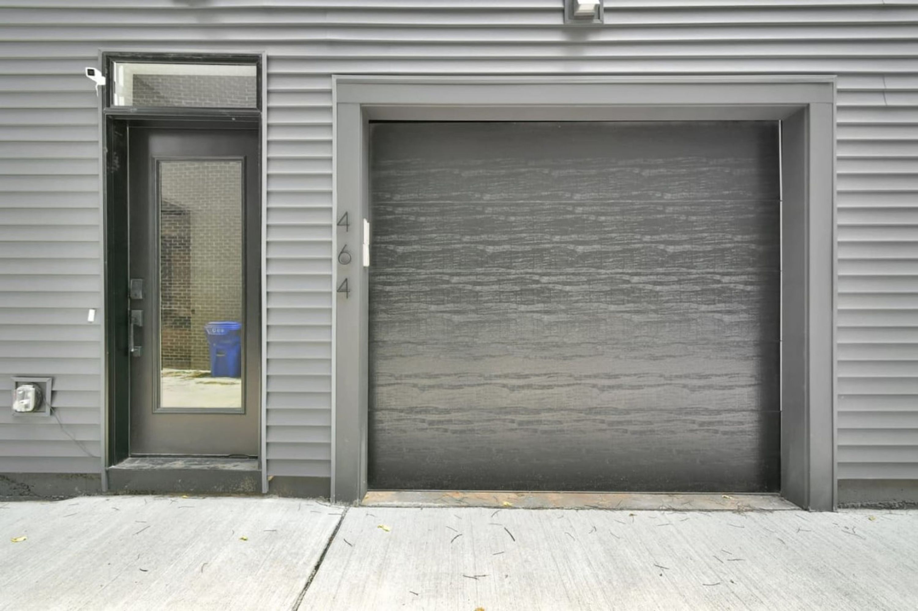 Een grijze metalen garagepoort met het cijfer '464' op de muur ernaast.