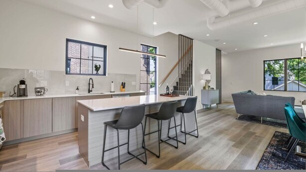 Une cuisine moderne dotée d’un îlot central, de tabourets de bar, d’un escalier et d’un espace de vie comprenant un canapé et des fauteuils.