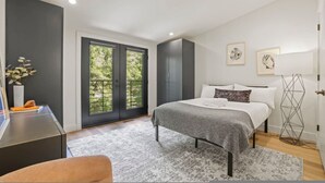 Une chambre à coucher comprenant un lit, un bureau, une chaise, une lampe sur pied et une fenêtre donnant sur un paysage verdoyant.