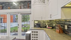 A modern kitchen with white cabinetry, a black and gray backsplash, and a coffee maker on the counter. - Franklin Manor-columbus Downtown Luxury Estate (Columbus)
