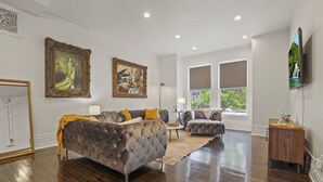 A spacious living room with a large sofa, a smaller sofa, and a coffee table. There are two large windows with curtains, a painting on the wall, and a wooden cabinet. - Franklin Manor-columbus Downtown Luxury Estate (Columbus)